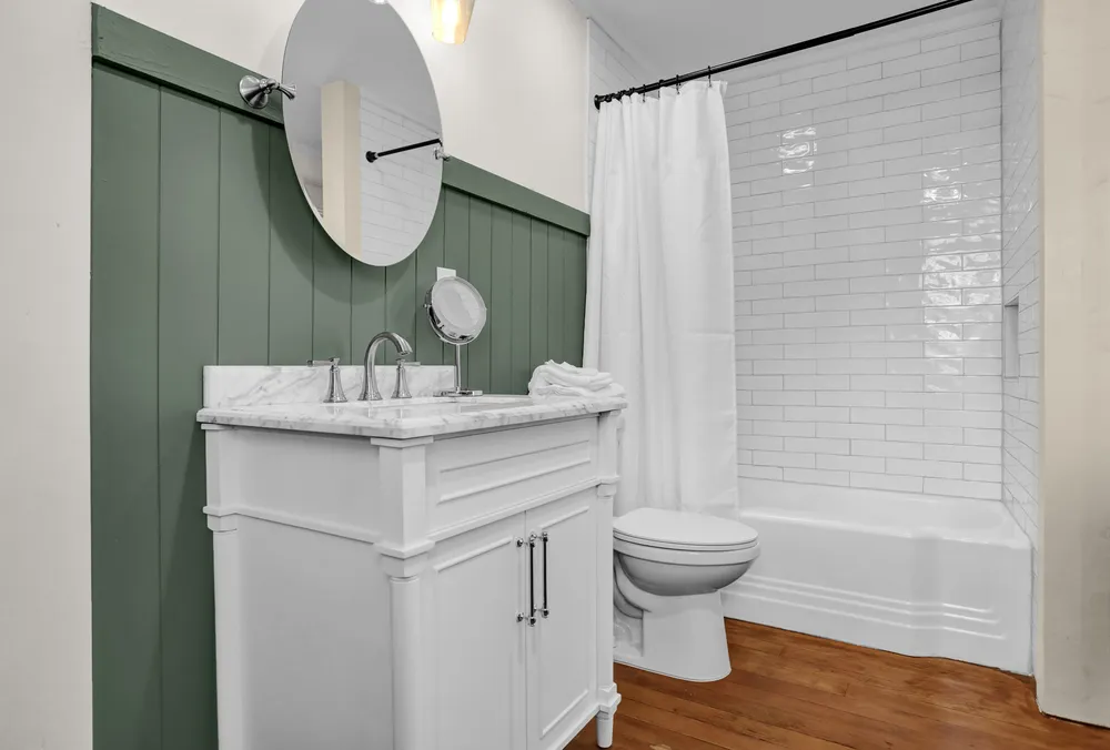 A bathroom with green panelling, a white vanity and a tub with shower.