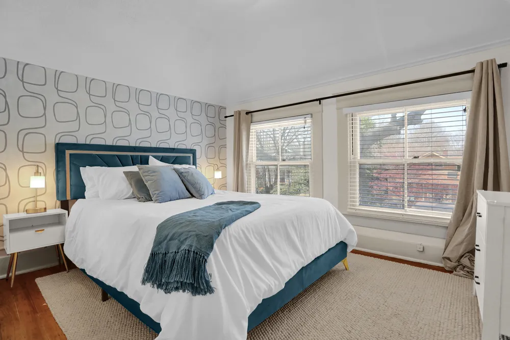 A bedroom with a teal headboard and two windows.