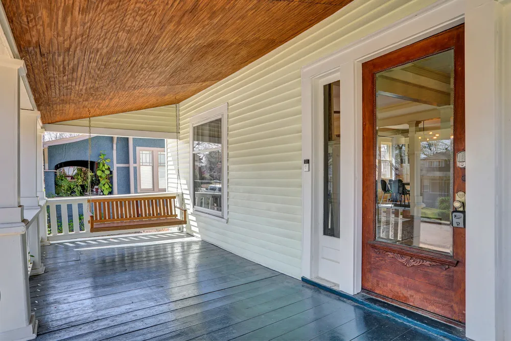 The covered front porch with a wooden swing and the front door.